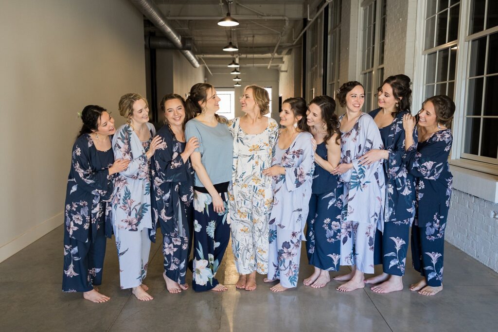Bride beaming with joy as her bridesmaids help her with the final touches, clad in comfy pajamas at the bridal suite, Judson Mill, Greenville, SC