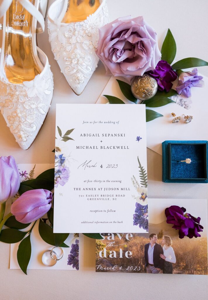 A beautifully arranged bridal detail flatlay showcasing the wedding invitation suite at Judson Mill in downtown Greenville, South Carolina. Delicate floral motifs and elegant typography adorn the invitation, setting the tone for an unforgettable wedding celebration