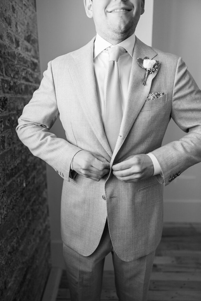 Groom's anticipation captured as he flawlessly buttons his jacket, adding the finishing touch to his stylish ensemble at Judson Mill wedding venue in Greenville, South Carolina.