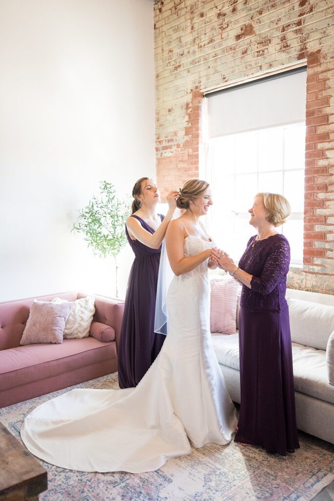 Sister's loving touch as she carefully places the bride's ethereal veil, adding the final touch to her bridal ensemble at Judson Mill, Greenville.