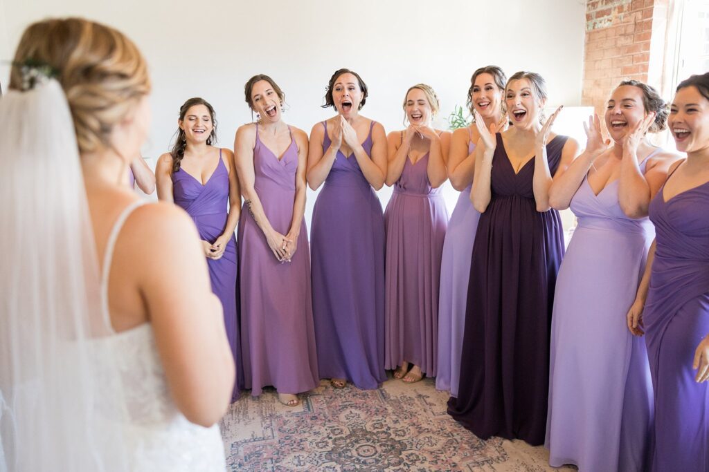 The bridesmaids' faces light up with sheer happiness and excitement as they catch their first glimpse of the stunning bride at Judson Mill, downtown Greenville, South Carolina.