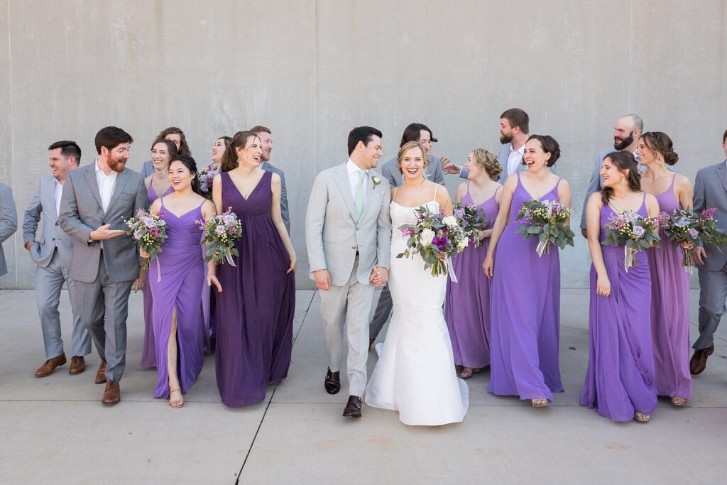 A heartwarming scene capturing the entire bridal party, including the radiant bride and groom, gathered together in front of the historic Judson Mill in downtown Greenville, South Carolina, commemorating a day filled with love and cherished memories.