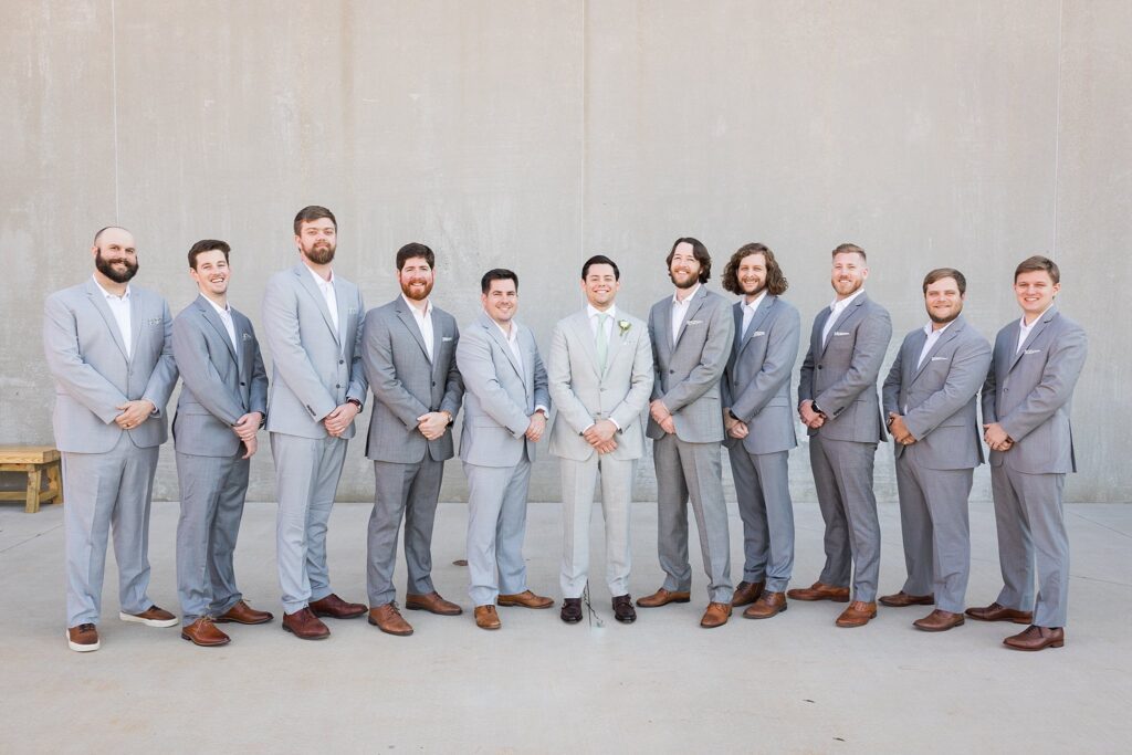 The groom leads his group of groomsmen with an air of confidence and happiness, their serious yet joyful expressions mirroring the significance of the occasion at Judson Mill in downtown Greenville, South Carolina.
