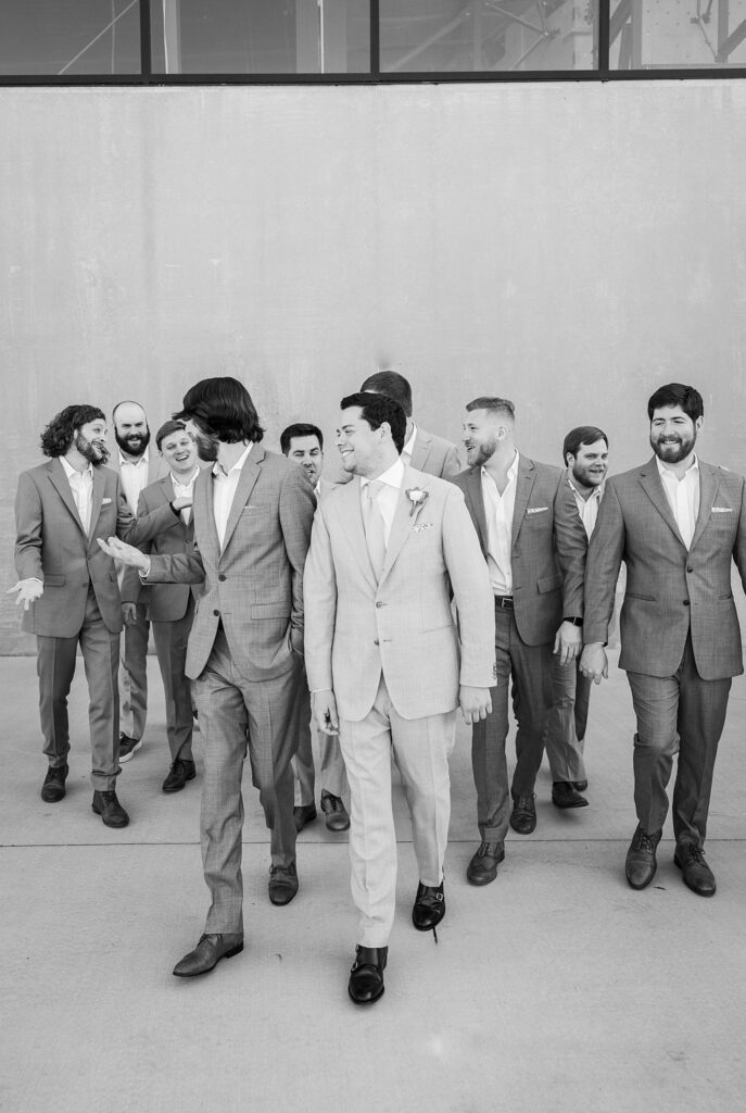 Groom walking confidently with his groomsmen, exuding pure joy on their special day at Judson Mill in downtown Greenville, South Carolina.