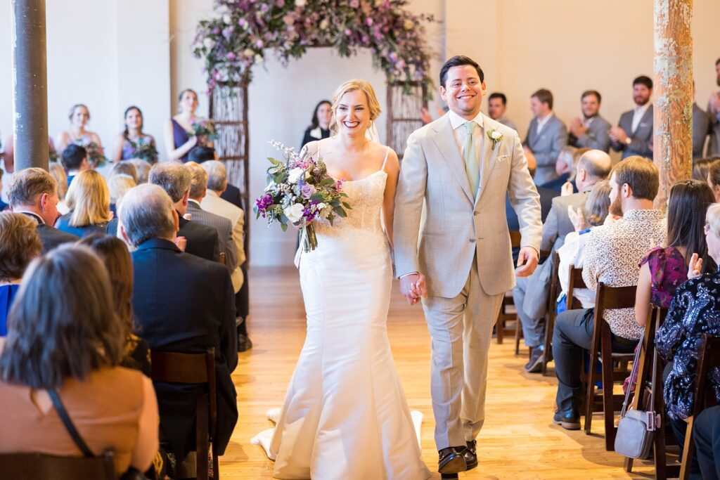 A joyful newlywed couple shares a tender moment, savoring the excitement of their union as they walk back up the aisle at their beautiful Judson Mill wedding in downtown Greenville, South Carolina.