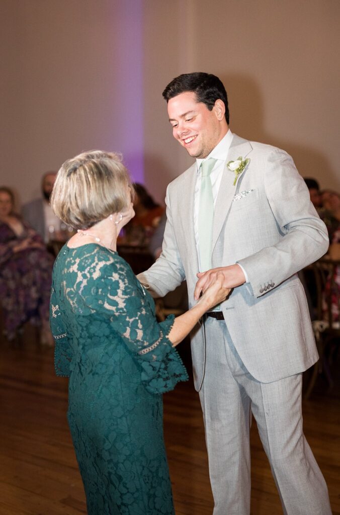 A heartwarming moment captured as the groom shares a tender dance with his loving mother at the reception held at Judson Mill, Greenville, South Carolina.