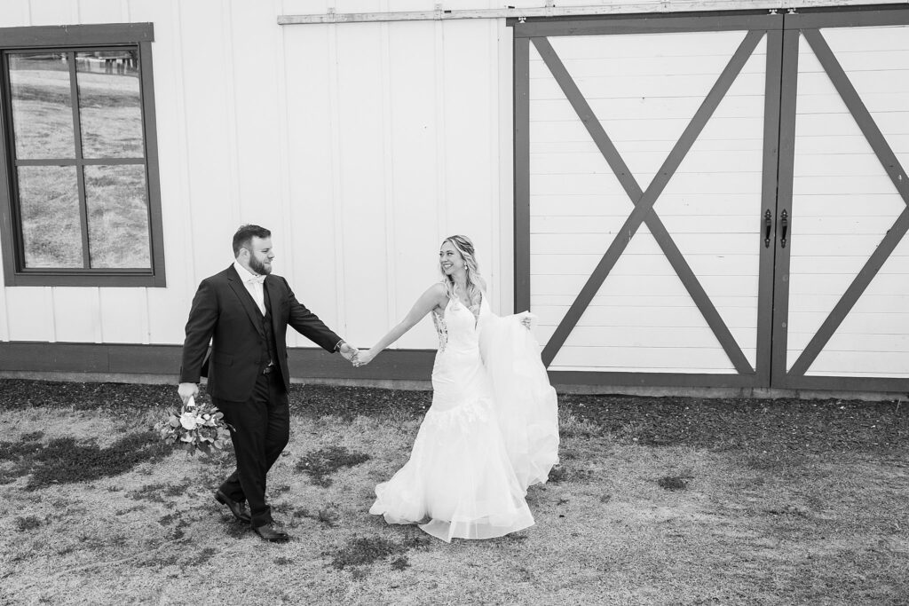 Love in the Air: Bride and Groom Walking at South Wind Ranch - The reception barn providing a charming backdrop for their love