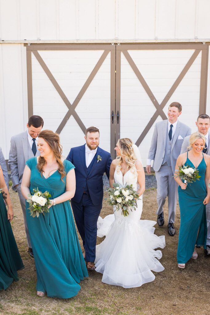 Unified Bridal Party: Bride and Groom Walking Hand in Hand at South Wind Ranch - A beautiful moment of togetherness with their loving bridal party