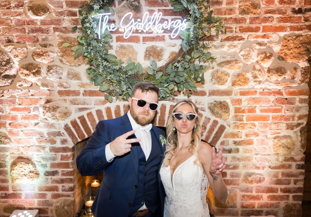 Sun-Kissed Memories: Bride and Groom Posing with Wedding-Branded Sunglasses at the Reception Headtable - Embracing the fun and stylish essence of their wedding day.