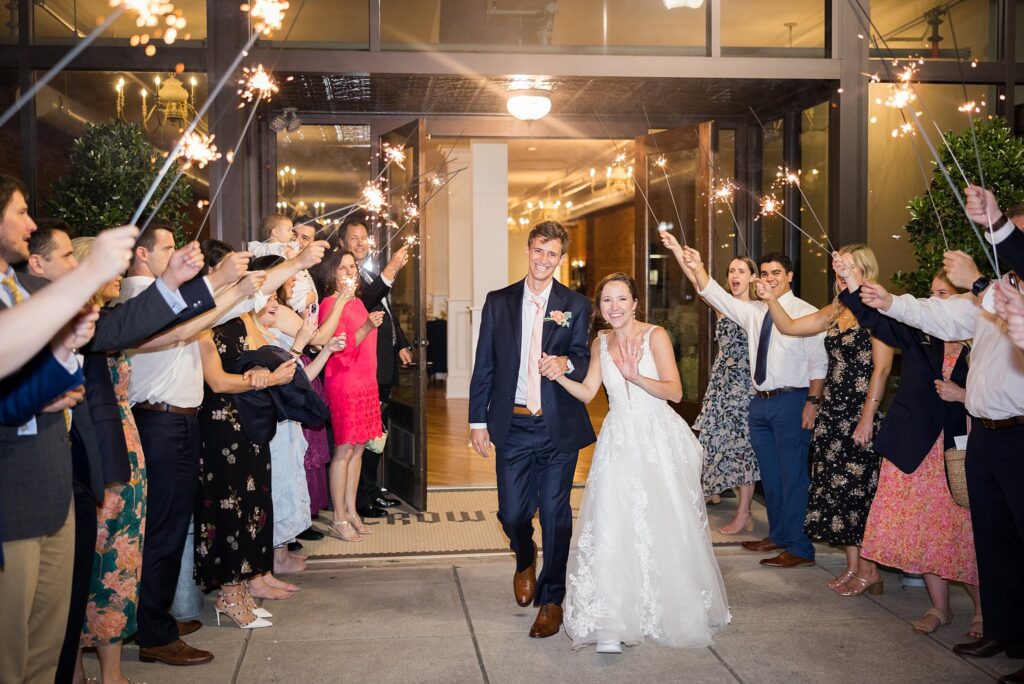 Candid laughter and joy captured among the shimmering lights of sparklers during a memorable sendoff at Crown and Crest by Lace + Honey Weddings.